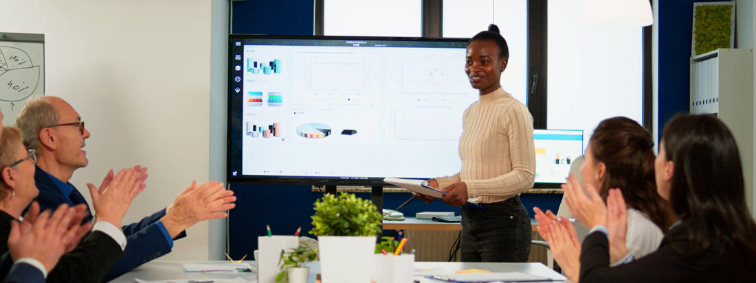 Audience applauds a presenter in a conference room in front of a screen.