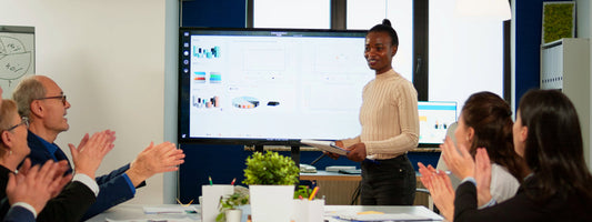 Audience applauds a presenter in a conference room in front of a screen.