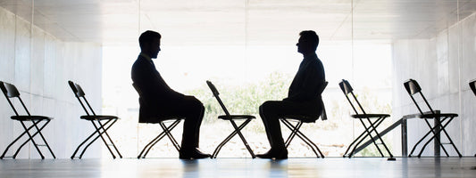Two men sit in front of one another in a conference room.