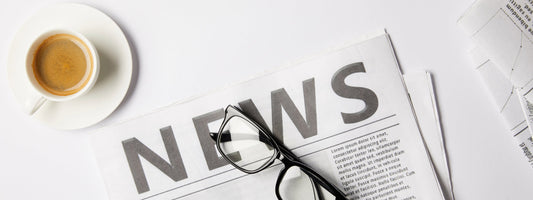 Coffee cup above a news paper with glasses on top of it.