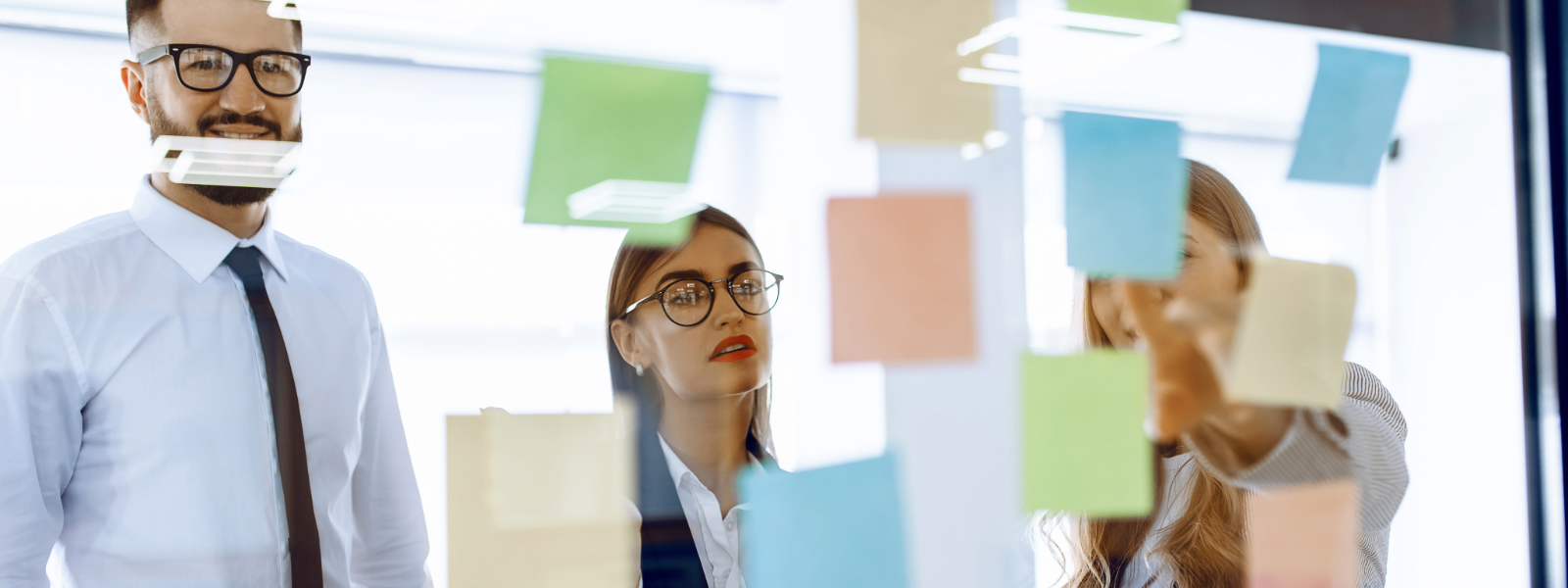 A handful of coworkers look at a board filled with post it notes.