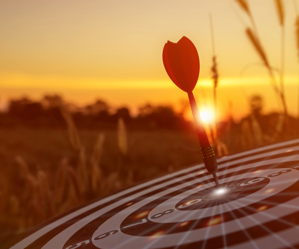 A dart hitting the center of a target on a sunset background