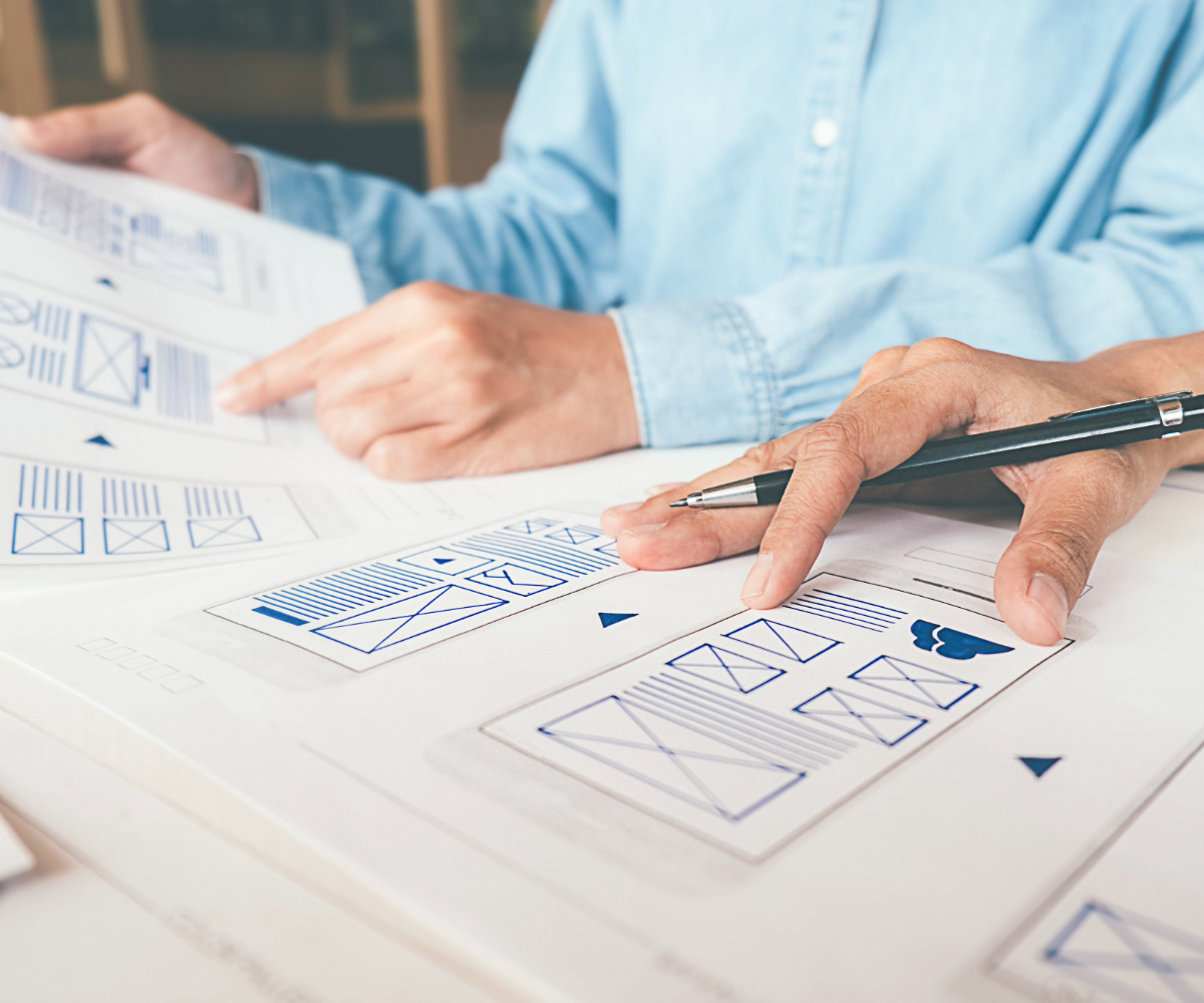 Wireframe on a table printed out with a man holding a pen on top of it.
