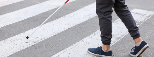 A blind person walks on a crosswalk with his or her cane showing a close up of their shoes.