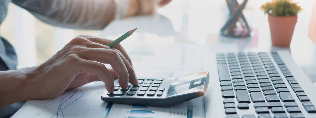 A hand typing on a calculator in front of a keyboard.