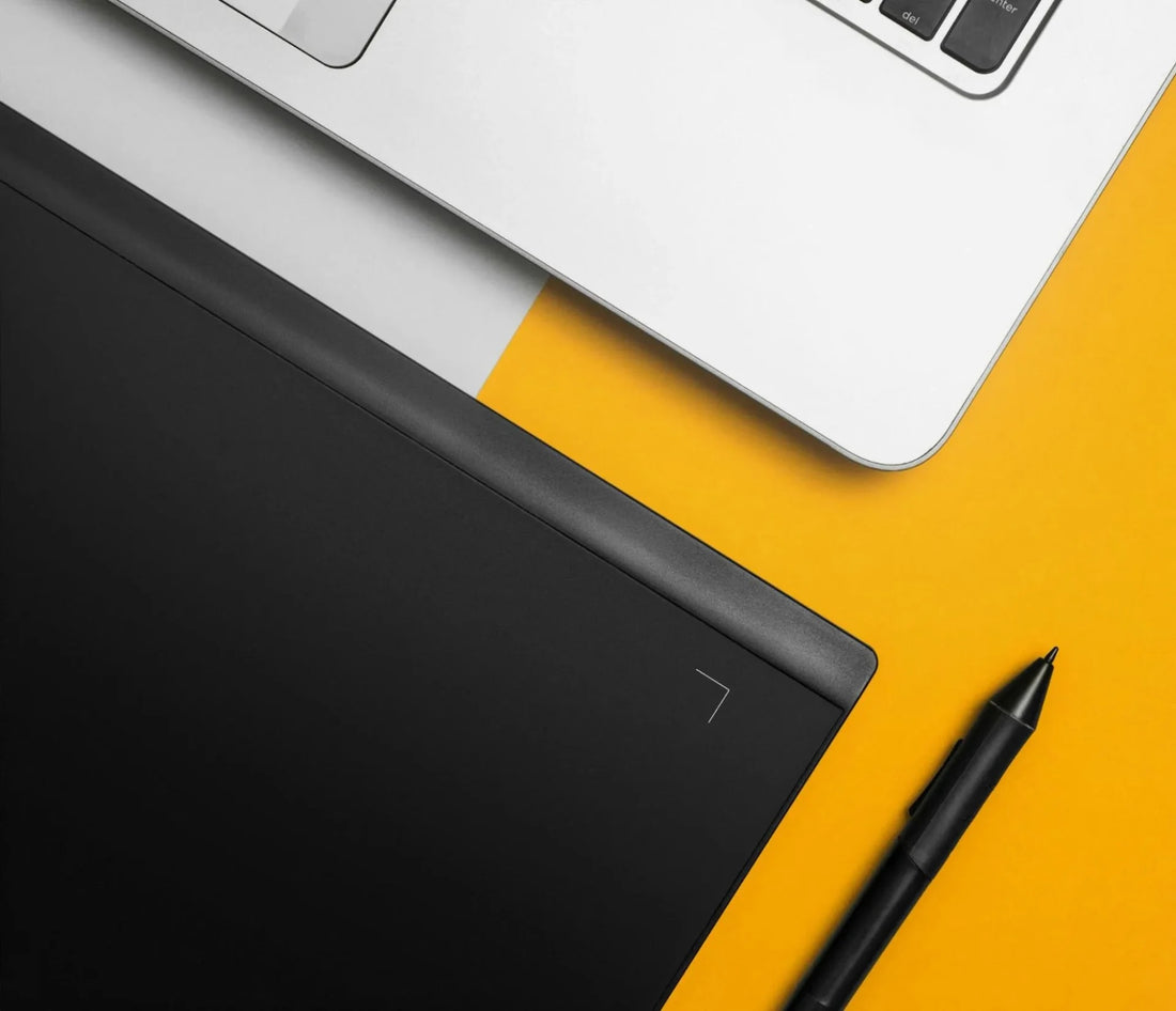 A corner of a laptop and ipad on a yellow background with a design pen.