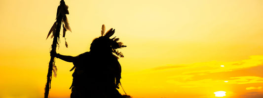 A native American stands watching the sun set.