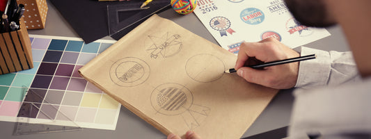 A man draws a few logos by hand on paper while looking at printed examples.