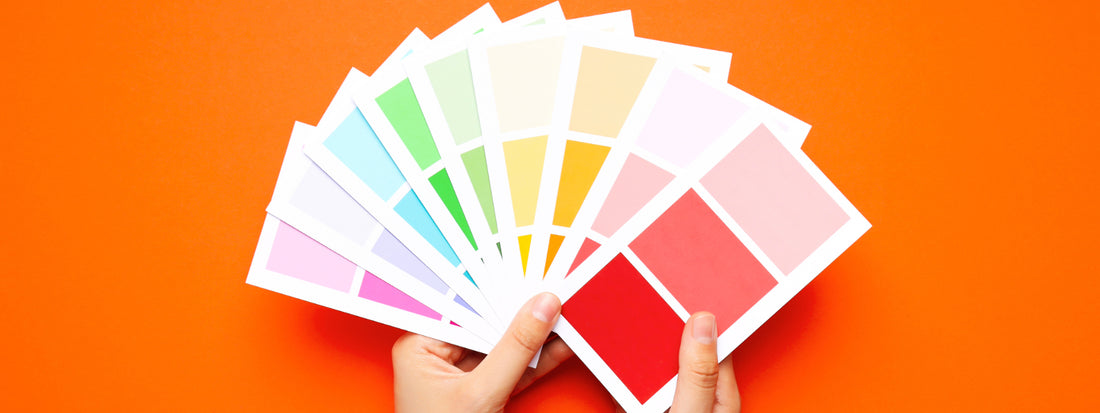 Pantone colors being held by a pair of hands on an orange background.