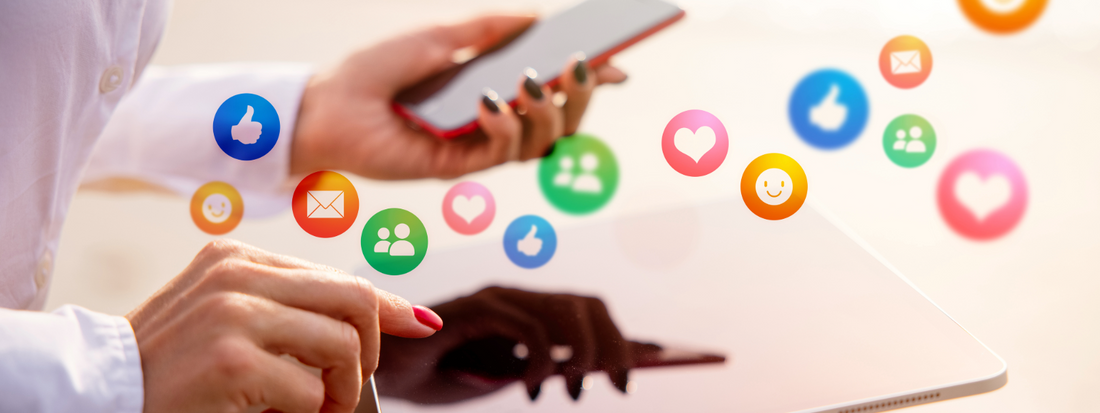 A woman holding a phone and iPad with a handful of social media engagements floating around of all different colors.