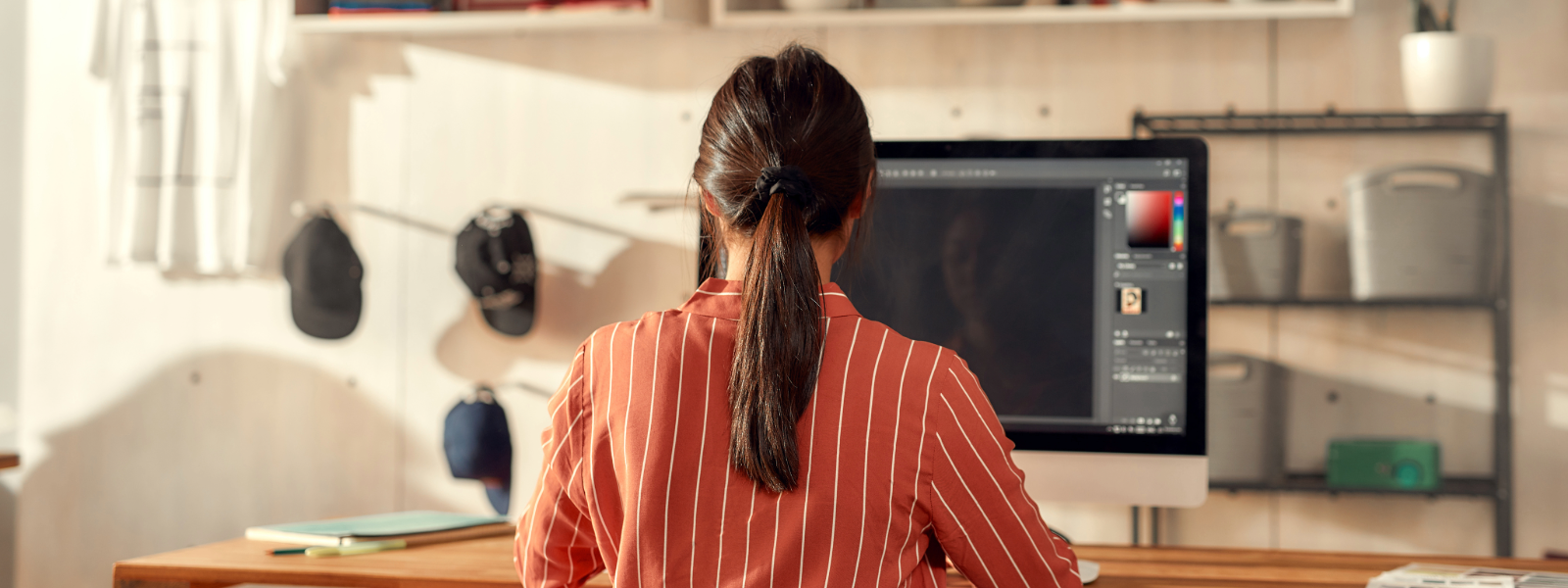 Woman designer in a red shirt sitting in front of Adobe Illustrator about to design a logo